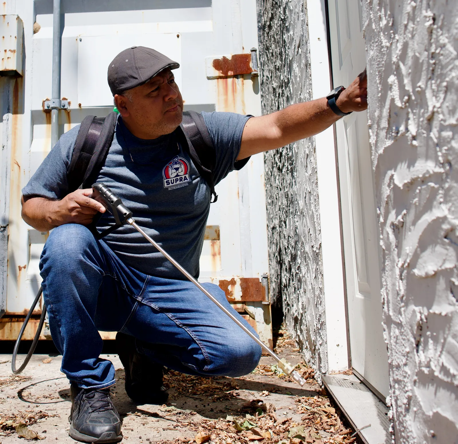 Supra Exterminator technician treating an exterior door and wall with a sprayer wand to block pest entry points